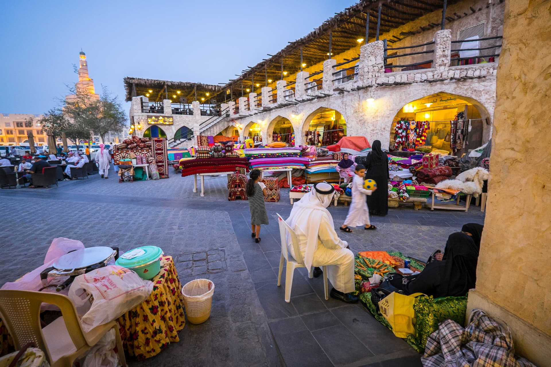 Stalls and shoppers in Souq Waqif at dusk, the Fanar minaret beyond