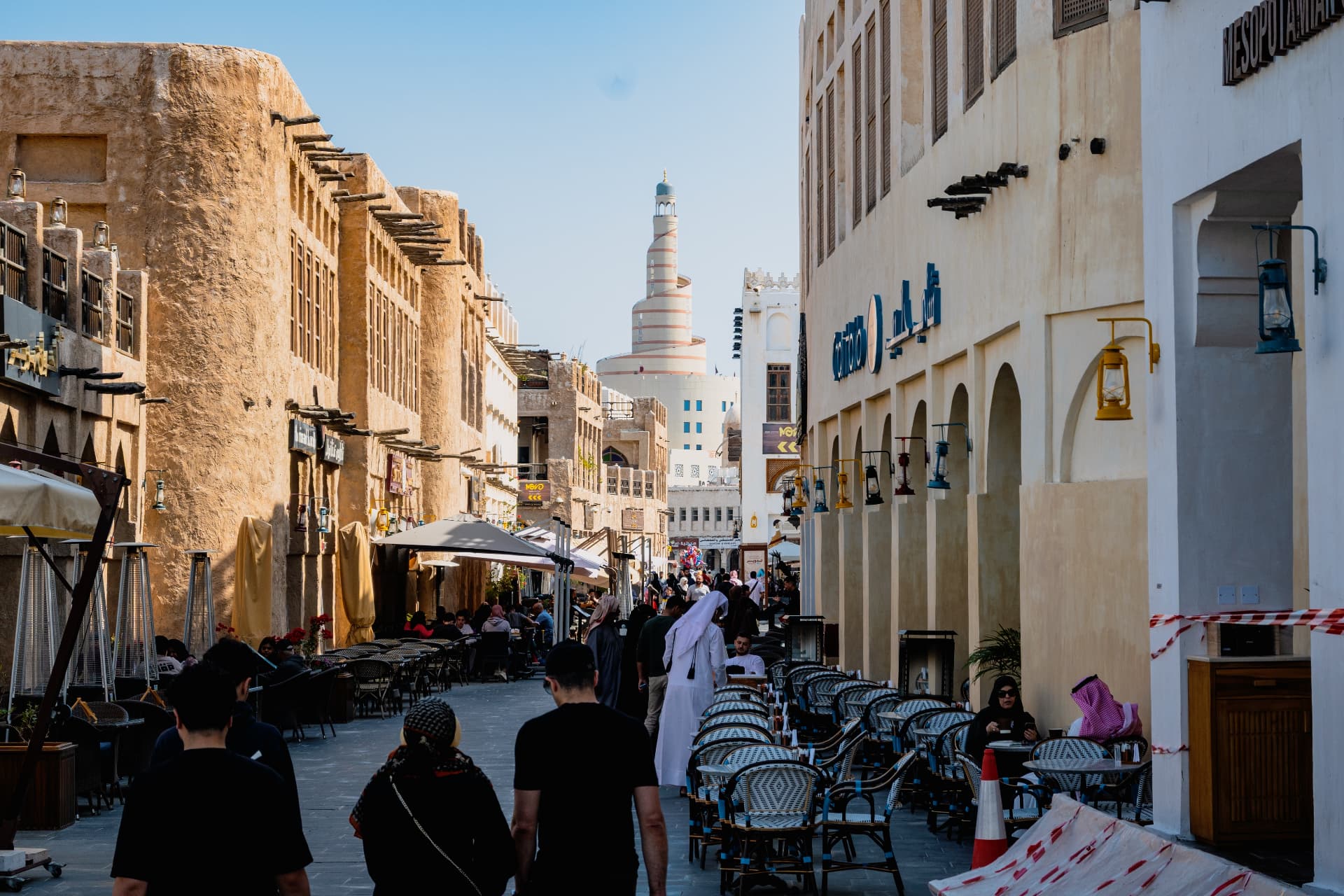 Café tables along a Souq Waqif lane beneath the Fanar spiral minaret